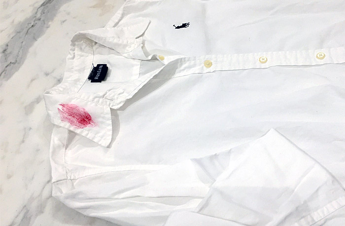 Removing lipstick stains from clothing. A white shirt laid out on a marble countertop with a red lipstick stain on the collar about to be laundered.