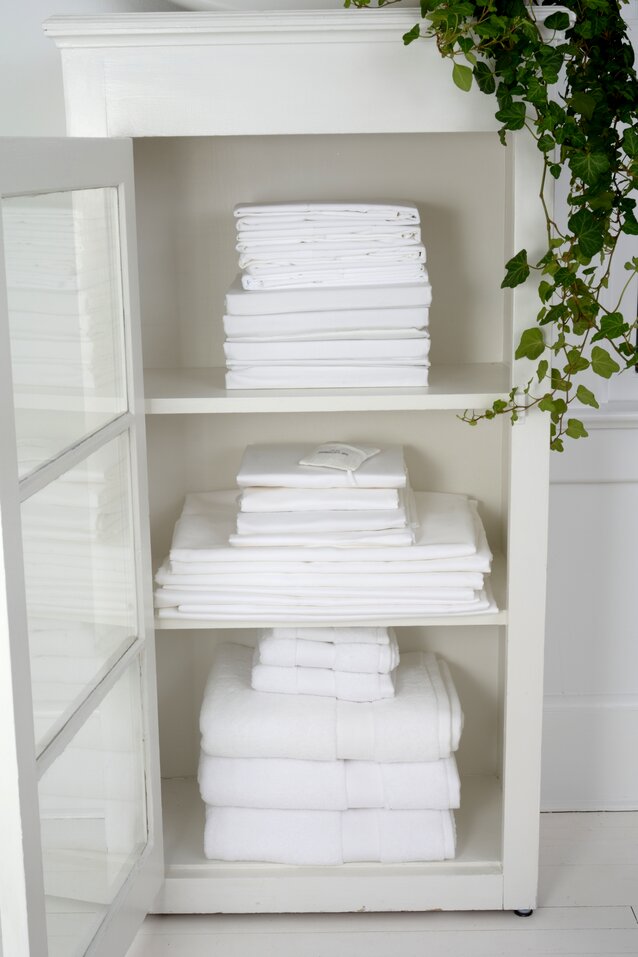 Neatly Stored Linens Shelves in a white cabinet holding neatly folded white linens