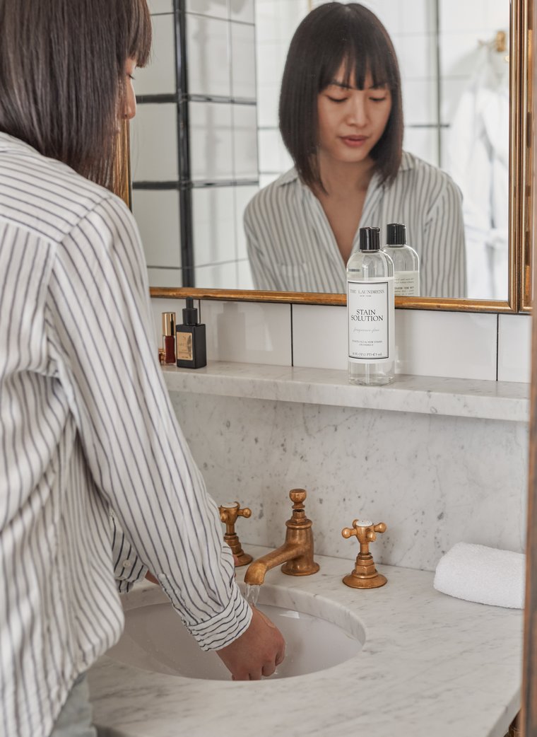 Cleaning process with Stain Solution A woman stands at a sink handwashing an item with The Laundress Stain Solution.