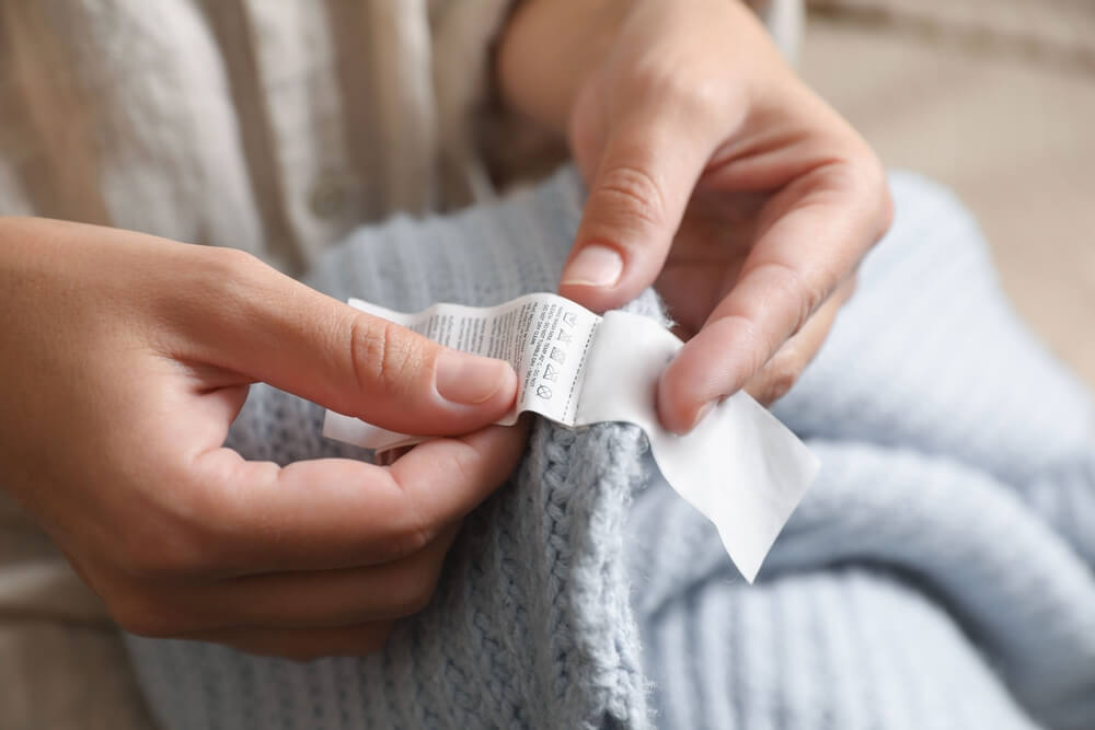 shutterstock_2275857565-1 A person checks a garment care label on a piece of clothing.
