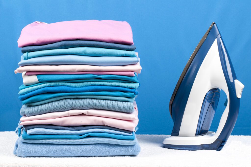 shutterstock_231456493-1024x680-1 An iron next to a stack of neatly folded towels.