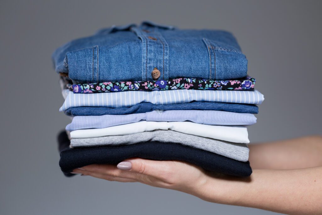 shutterstock_242700229-1024x683-1 Someone holding a stack of neatly folded clothes.